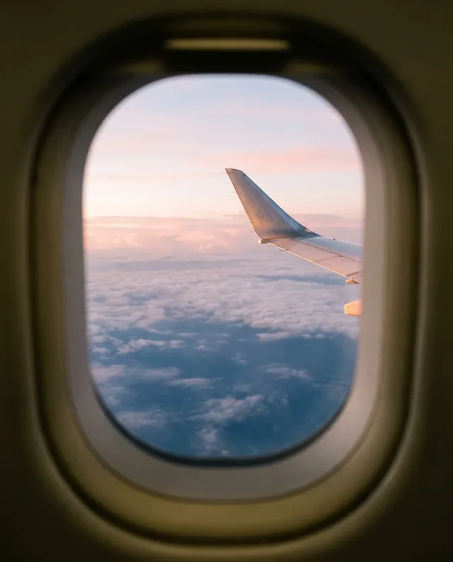 Die Tragfläche eines Flugzeugs über den Wolken im Morgengrauen, durch ein Kabinenfenster gesehen.